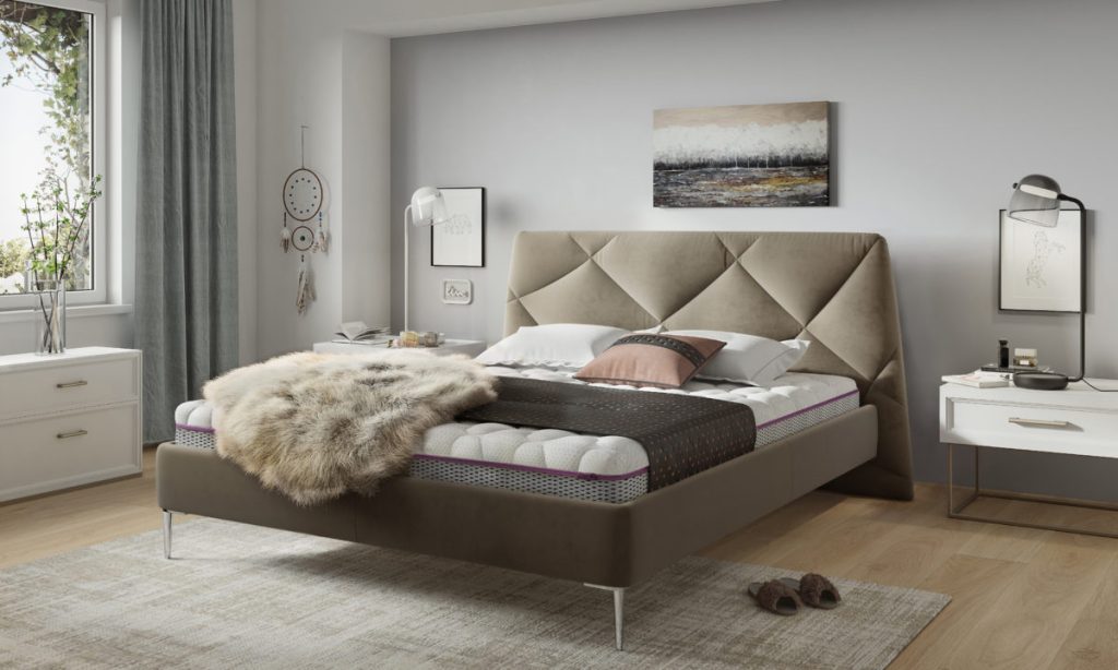 Łóżko tapicerowane Davos. Wezgłowie w kształcie przypominającym trapez. Podstawa łóżka znajduje się na wyższych nóżkach. Producent Comforteo